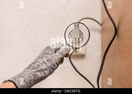 La main d'un ouvrier de construction masculin en gants de protection examine à travers une loupe la connexion des appareils dans la maison. Banque D'Images