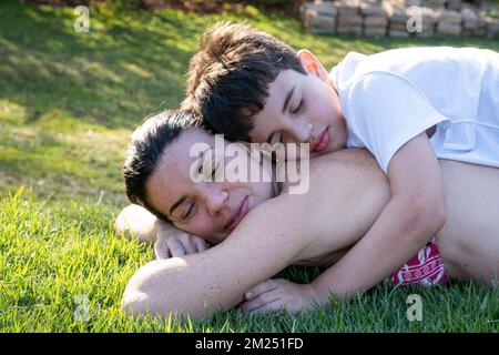 Gros plan de la mère brésilienne et de son fils avec les yeux fermés, allongé sur la pelouse dans un après-midi ensoleillé. Banque D'Images