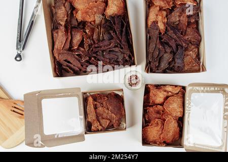 Certaines boîtes en carton de spécialité avec des friandises déshydratées pour chiens, la plus haute est ouverte, pleine de viande sèche croquante goûts de boeuf et de poulet. Animal de compagnie fait maison Banque D'Images