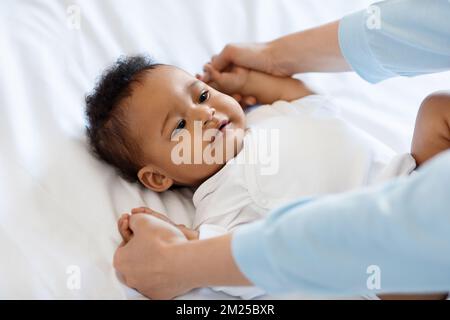 Mère méconnaissable faisant de la gymnastique avec mignon petit bébé noir couché sur le lit Banque D'Images