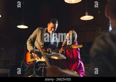 Le POV du batteur pendant un concert. Batteur masculin flou avec des bâtons en bois au premier plan, regardant la chanteuse caucasienne et le guitariste mâle. Prise de vue en intérieur. Photo de haute qualité Banque D'Images