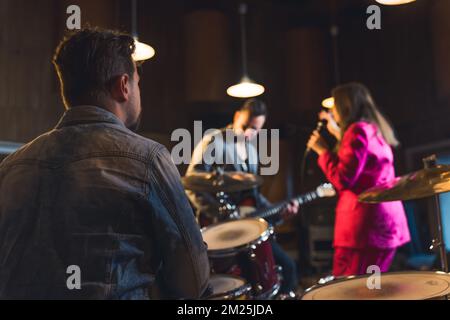 Vue du batteur lors d'un concert de répétition. Vue arrière du batteur masculin regardant le chanteur et le guitariste. Arrière-plan flou. Prise de vue en intérieur. Photo de haute qualité Banque D'Images