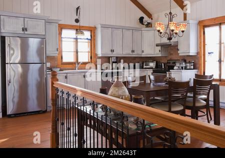 Armoires en bois blanchi et table à manger avec chaises à dossier haut dans l'extension intérieure de la cuisine attachée à la vieille maison en pierre de champ de style cottage Canadiana. Banque D'Images