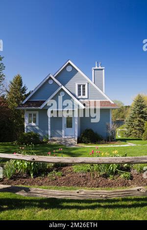 Petit bleu avec garniture blanche maison de deux étages et bordure de tulipe protégée par une clôture de perchoir au printemps. Banque D'Images