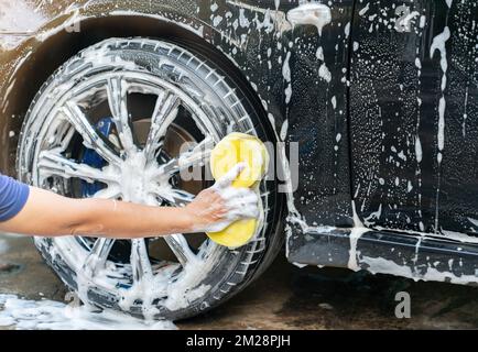 Le service de voiture lave les roues de voiture avec une éponge jaune à l'extérieur. Détails de voiture. Banque D'Images