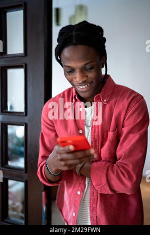 Jeune homme afro-américain heureux tenant un smartphone discutant avec une petite amie à la maison Banque D'Images