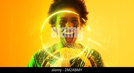 Fan afro-américain avec balle et visage brésilien peint criant par les plantes et le cercle Banque D'Images