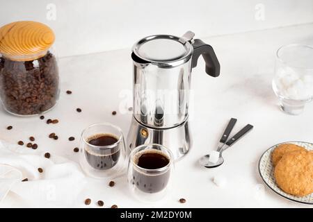 Machine à café geyser, verre d'espresso, bol avec haricots et assiette avec biscuits sur la table Banque D'Images