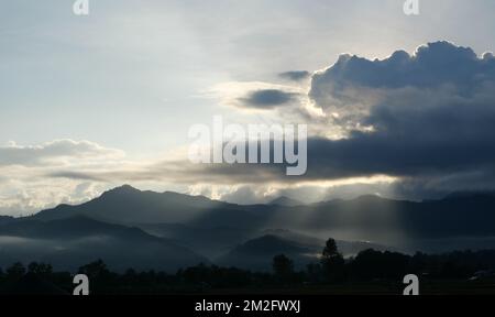 Silhouette d'arbre et de montagne avec la lumière de sunbeam pousse à travers le nuage sombre jusqu'à la terre au lever du soleil, Mist couvre la forêt et les montagnes à l'aube Banque D'Images