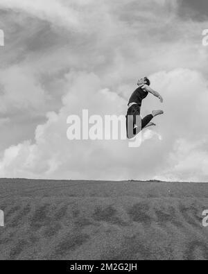 Homme sautant au-dessus du désert de sable. Noir et blanc Banque D'Images