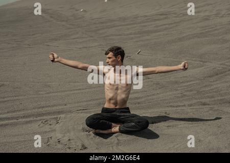 Homme assis sur la dune de sable et versant du sable à la main dans le désert Banque D'Images