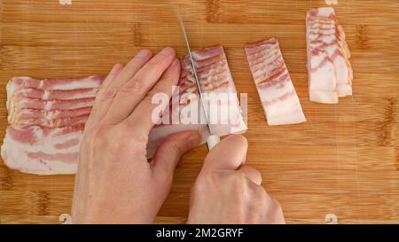 La femme coupe le bacon en tranches. Vue rapprochée depuis le dessus, arrière-plan en bois Banque D'Images