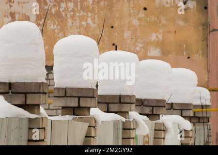 Belles, même, hautes colonnes de neige sur des piliers de briques. Une rangée régulière de petites chutes de neige se déforme sur le fond d'un mur de merde. Paysage urbain d'hiver. Jour d'hiver nuageux, lumière douce. Banque D'Images