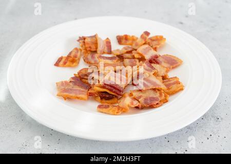 Tranches de bacon frites croustillantes sur une plaque blanche en gros plan sur fond gris clair Banque D'Images