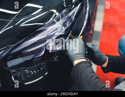 Deux mains dans des gants de protection en caoutchouc noir recouvrant le phare du véhicule d'un film pour les assombrir. Gros plan en intérieur. Détails de voiture. Photo de haute qualité Banque D'Images