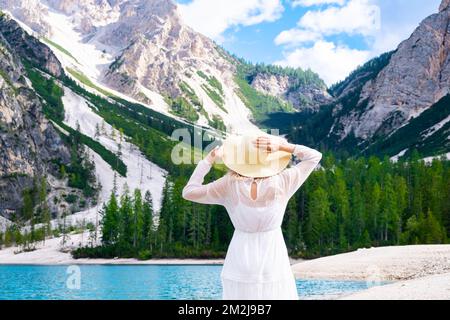 Belle femme vêtue d'une robe blanche marchant sur les rives du lac Braies avec une vue incroyable sur les alpes. Banque D'Images