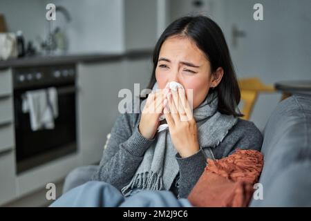 Portrait d'une jeune femme coréenne malade se sentant malade, éternuant et tenant une serviette, restant malade à la maison, attrapée par le froid Banque D'Images