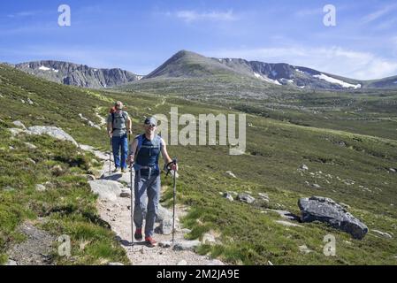 Deux randonneurs / alpinistes avec des bâtons de marche et des sacs à dos en descendant le chemin de montagne au printemps dans le parc national de Cairngorms, Highland, Écosse | propriétaires dans le parc national de Cairngorms, Ecosse, Royaume-Uni 09/06/2018 Banque D'Images