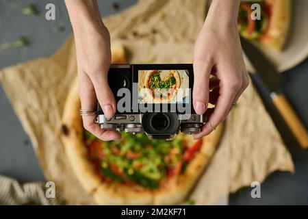 Vue en grand angle d'une femme qui prend des photos de pizza maison avec un appareil photo numérique Banque D'Images