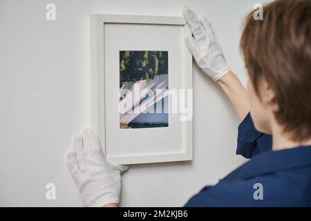 Vue arrière d'une jeune femme décorant un mur blanc avec photo encadrée Banque D'Images