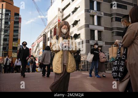 Yokohama, Japon. 18th novembre 2022. Une jeune femme regarde son téléphone mobile tout en traversant le pont de Nanko près de la gare de Yokohama. Crédit : SOPA Images Limited/Alamy Live News Banque D'Images