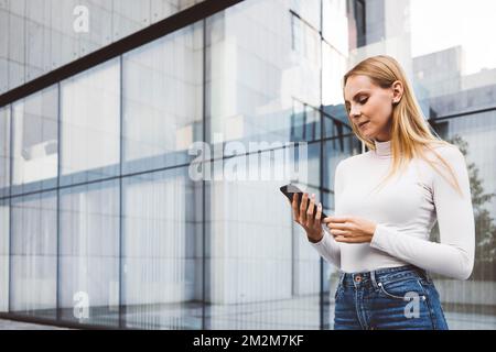 Taille haute femme en milieu urbain debout à l'extérieur regardant son téléphone Banque D'Images