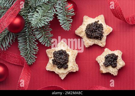 Caviar noir hors-d'œuvre le pain étoiles sur un fond rouge décoré de noël horizontal Banque D'Images
