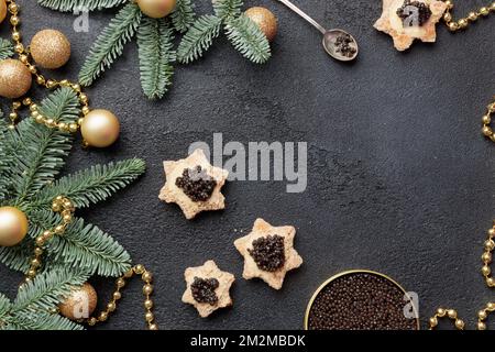Caviar noir hors-d'œuvre étoiles sur une table noire décorée de noël Copyspace horizontal Banque D'Images