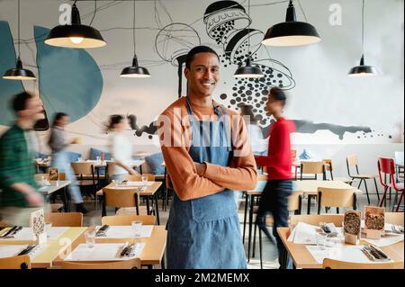 portrait d'un propriétaire ou d'un serveur souriant dans un café avec des employés flous non reconnaissables en mouvement. Banque D'Images