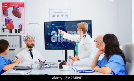 Femme âgée chercheuse utilisant la haute technologie médicale analysant l'impulsion du cerveau dans la salle de conférence, assistant testant de nouvelles innovations. Médecins étudiant le diagnostic pour le traitement des patients travaillant à l'hôpital Banque D'Images