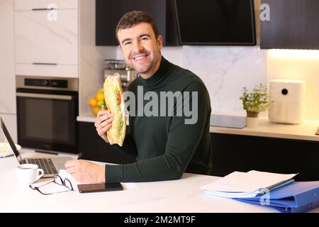 Employé mangeant un très grand sandwich dans le bureau à la maison Banque D'Images