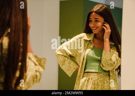 Jeune belle femme souriante aux cheveux longs posant dans le miroir à la maison Banque D'Images