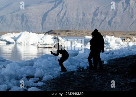 On voit des gens marcher près des zones de glace sur la rive du lac Jökulsárlón. Jökulsárlón est un lac situé dans le sud de l'Islande, avec une superficie de 20 km2 et une profondeur de plus de 200 mètres. Jusqu'à il y a moins de 100 ans, le glacier de Breiðamerkurjökull (qui fait partie du glacier Vatnajökull) s'étendait même au-delà du périphérique. En raison de la hausse des températures, le glacier a reculé, créant cette impressionnante lagune glaciaire. Banque D'Images