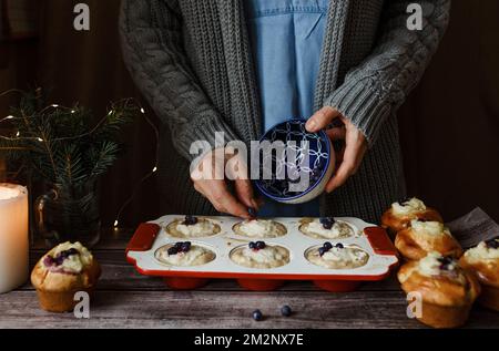 Gros plan des mains de femmes remplissant des moules de cupcake avec des ingrédients de pâte, une table de fête. Accessoires de cuisine Banque D'Images