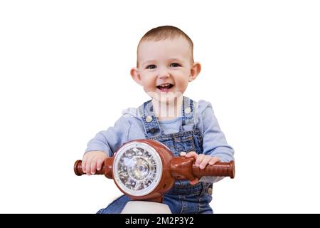 Un bébé joyeux, isolé sur fond blanc, fait une moto en plastique pour enfants dans la salle de jeux. Un enfant souriant conduit un jouet de mobylette, isolé sur un Banque D'Images