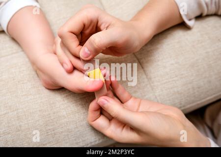 La mère colle un pansement médical adhésif sur la jambe du bébé. Main de maman avec ruban adhésif de protection collant et pied d'enfant. Enfant âgé de un vous Banque D'Images