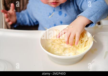 Drôle d'enfant manger une pomme râpée avec sa main d'une assiette, gros plan. Bébé garçon affamé mange des fruits, de l'humour. Enfant âgé d'un an et trois mois Banque D'Images