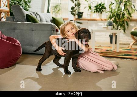 Petite fille mignonne, enfant jouant avec un chien de race, Labrador brun à la maison. Adorables câlins. Animal préféré Banque D'Images