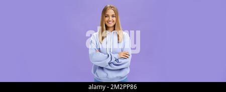 Portrait de charmante femme européenne charismatique avec la peau bronzée dedans un sweat à capuche tendance de grande taille se croisant les mains contre la poitrine en souriant largement appareil photo Banque D'Images