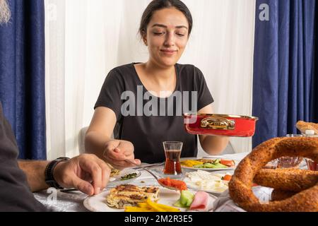 Portrait de la femme servant de la nourriture petit déjeuner familial. Routine traditionnelle turque matinale à la maison. Thé, patty appelée su borek, bagel appelé SIMIT, fromage. Banque D'Images