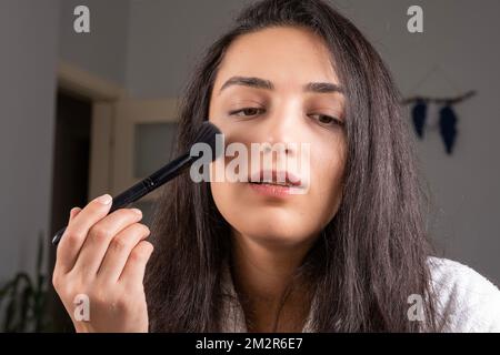 Belle brunette caucasienne fille tenant la brosse de maquillage. Rafraîchir son maquillage pour la nuit. Ouvrez doucement la bouche. Profitez de sa peau et de sa beauté. Banque D'Images