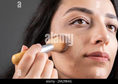 Image rapprochée d'une femme attrayante appliquant une fondation tonale liquide. Tenir et utiliser la brosse pour faire son propre maquillage. Idée de concept de soins de la peau. Banque D'Images
