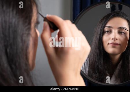 Vue rapprochée de l'épaule d'une femme tenant la brosse pour sourcils. Brunette, caucasienne, femme millénaire avec miroir parfait pour le maquillage. Idée de soin de la peau. Banque D'Images