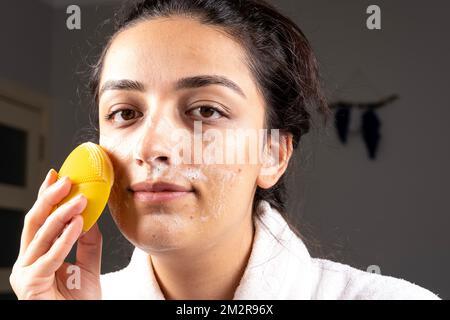 Femme du caucase du millénaire nettoyant la peau du visage avec une éponge et de la mousse. Concept d'auto-soin de la peau à la maison. Porter un peignoir. Idée de traitement d'acné de visage. Banque D'Images