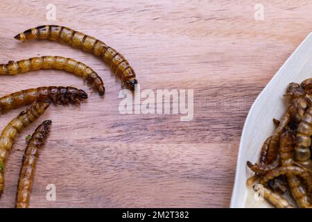 Vers de bois frits et vers de viande sur une planche à découper en bois. Insectes frits comme source de protéines dans le régime. Banque D'Images