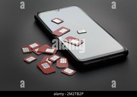 Smartphone et beaucoup de cartes sim rouges sur fond gris, dans une touche sombre Banque D'Images