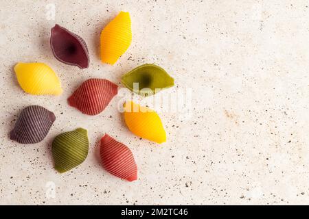 Coquilles de pâtes cinq couleurs sur fond de pierre blanche. Pâtes au curcuma, aux épinards, à la betterave et à la carotte noire. Banque D'Images