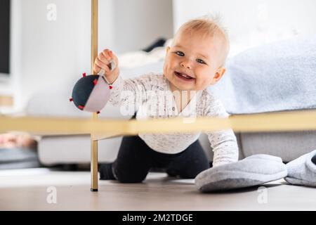 Mignon bébé garçon jouant avec le ballon suspendu, rampant et debout près de la table du salon à la maison. Centre d'activités et de jeux pour les jeunes enfants. Bébé jouant à la maison Banque D'Images