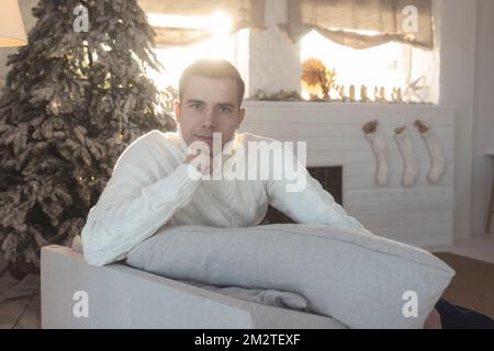 Un homme dans un chandail blanc sur le fond des décorations du nouvel an est assis dans un fauteuil Banque D'Images