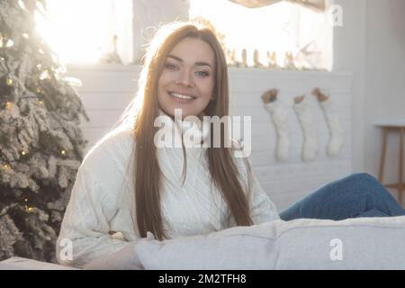 Belle fille dans un chandail blanc sur fond de décorations du nouvel an est assis dans une chaise Banque D'Images